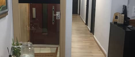 A hallway with wooden flooring, a white couch, a small table with decorative items, and a black desk with a computer.