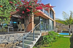 Ein modernes Haus mit einer Steinstufenanlage, einem Glasgeländer und einem Pool.