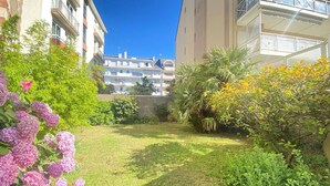 Un patio con césped, varios arbustos y un edificio con múltiples balcones.