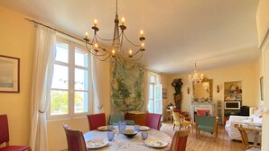 Un comedor con una mesa redonda dispuesta para cuatro personas, rodeada de sillas rojas. Un candelabro cuelga sobre la mesa, y se observa un cuadro en la pared detrás.