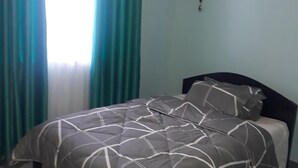 Un dormitorio con una cama, cortinas color verde azulado y una pared azul claro.