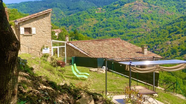 Una casa de piedra con techo de tejas, un tobogán verde y paneles solares.