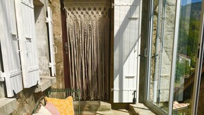 Un patio soleado con una zona de estar con cojines, un banco y una puerta con cortinas decorativas.