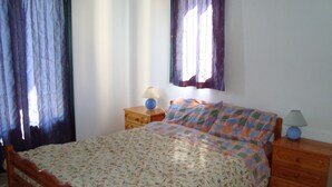 A bedroom with a wooden bed, floral bedding, two bedside tables with lamps, and curtains on the windows. - Apartment with a view (Palaia Epidavros)