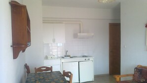 A compact kitchen with white cabinets, a sink, and a small stove. There is a dining table with chairs and a sofa in the living area. - Apartment with a view (Palaia Epidavros)