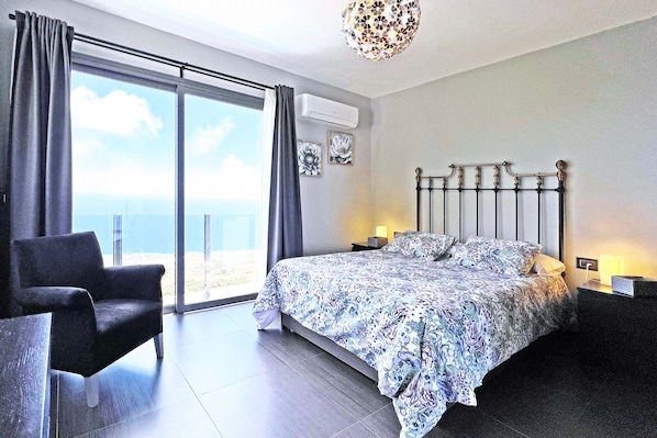 A bedroom with a bed, a chair, a nightstand, and a view of the sea. - Villa Gamonal en Tijarafe (Tijarafe)