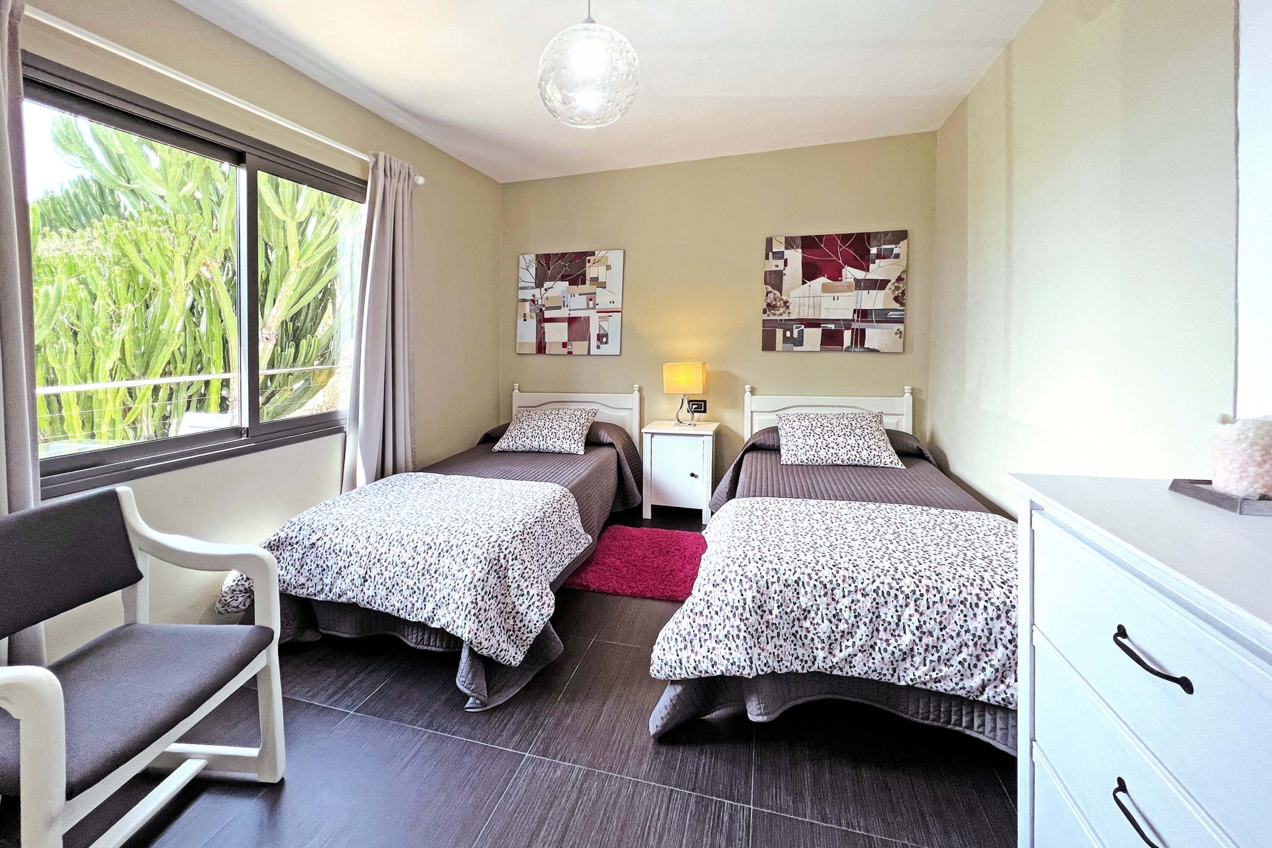 A room with two beds, a chair, a nightstand, a lamp, and artwork on the walls.