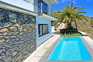 Ein modernes Haus mit Natursteinfassade, Schwimmbad und einer Palme.