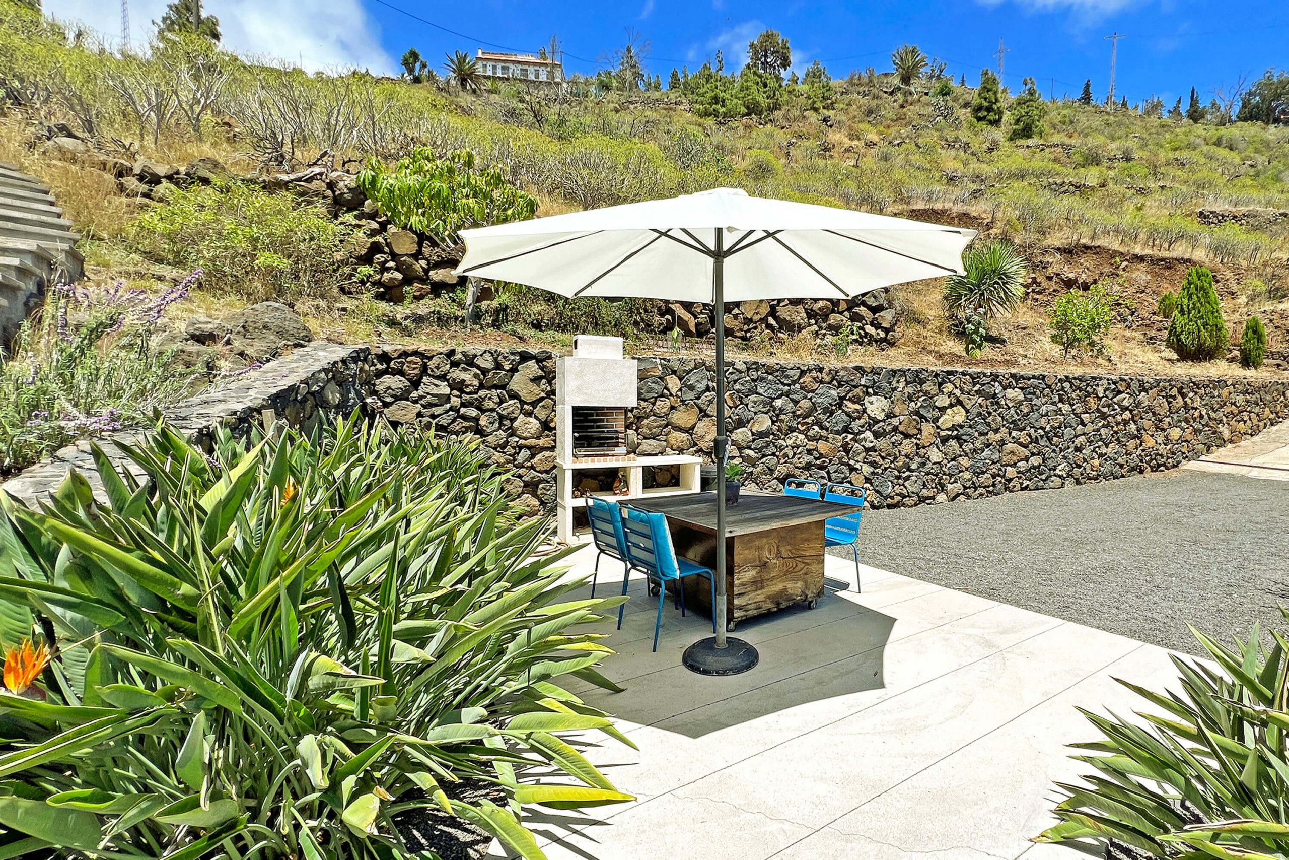Une terrasse extérieure avec une table et des chaises, un grand parasol et un mur en pierre.