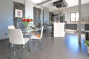 Eine moderne Küche mit Kochinsel, Essbereich mit Glastisch und Stühlen sowie eine Steinwand mit Kunstwerken.