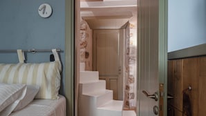 A bedroom with a bed, a wooden door, and a staircase leading to a door with a curtain.