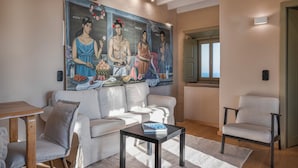 A living room with a white sofa, a small table, a chair, and a large mural on the wall.