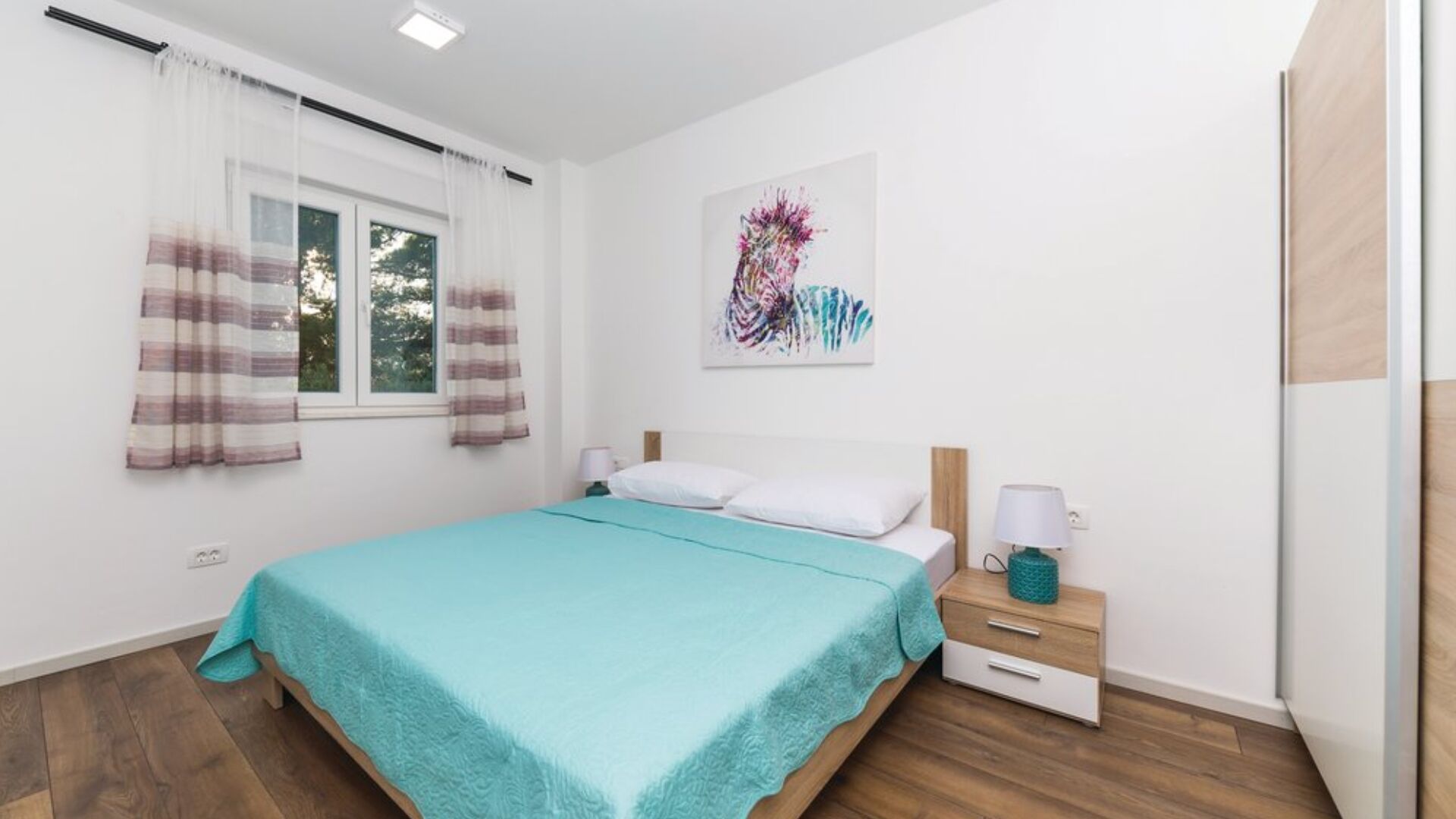 Un dormitorio con cama, mesita de noche, lámpara y ventana con cortinas.