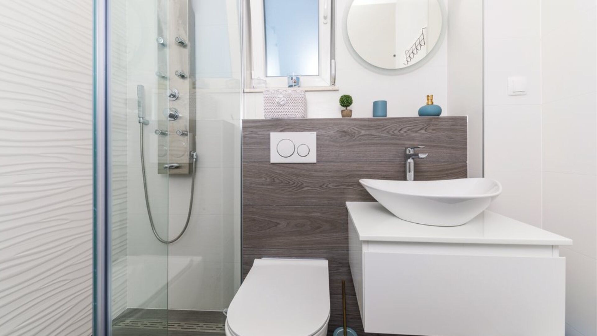Un baño moderno con cabina de ducha de vidrio, un lavabo blanco con lavamanos de diseño y un inodoro.