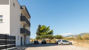 A modern building with a white facade, multiple balconies, and a parking area with cars. - Villa David (Kastel Lukšić)