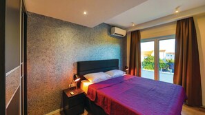 A bedroom with a large bed, a nightstand, an air conditioning unit, and a view of the outdoors through a sliding door. - Villa David (Kastel Lukšić)
