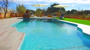 A swimming pool with tiled edges, surrounded by a wooden deck and a grassy area. There are lounge chairs and umbrellas in the background. - Son Antem 420 fantastic finca with private pool, terrace, barbecue and air conditioning (Llucmajor)