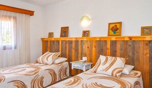 Ein Zimmer mit zwei Betten, einem Holz-Kopfteil, einem kleinen Nachttisch mit einer Schale und einer Wandlampe.