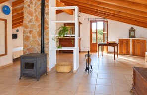 Une pièce chaleureuse avec un mur en pierre, un plafond en bois, une cheminée, une table en bois et une fenêtre.