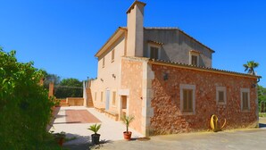 A two-story house with a stone facade, a chimney, and a small garden with potted plants. - Can Palea 407 finca with private pool with garden, terrace, barbecue and WiFi (Campos)