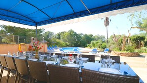An outdoor dining area with tables set for a meal, a pool in the background, and a covered seating area. - Can Palea 407 finca with private pool with garden, terrace, barbecue and WiFi (Campos)