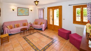 Una sala de estar acogedora con dos sofás, una mesa de centro y una alfombra. Hay puertas de madera que dan a un área exterior.