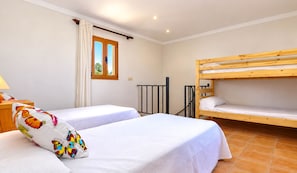 Una habitación con dos camas individuales, una litera, una ventana con cortinas y una lámpara en una mesita de noche.