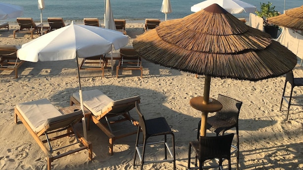 Een strand met rijen ligbedden en parasols, waarvan sommige voorzien zijn van rieten kappen, gericht op de zee.