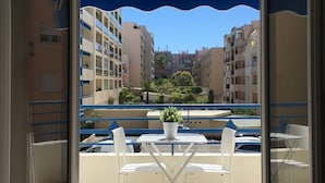 Een balkon met een tafel en stoelen, een bloempot en uitzicht op omliggende gebouwen.