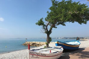 Uma praia com barcos, um molhe rochoso e céu claro.