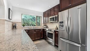Une cuisine moderne avec des meubles en bois foncé, des appareils électroménagers en acier inoxydable, un four à micro-ondes encastré et une grande fenêtre donnant sur un paysage verdoyant.