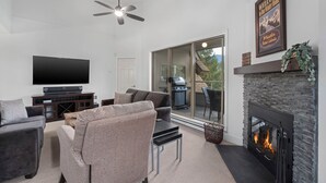 Un salon moderne doté d’un téléviseur à écran plat, de sièges confortables, d’une cheminée et d’un balcon avec un barbecue.
