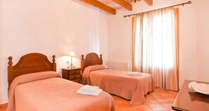 A hotel room with two wooden beds, a nightstand with a lamp, a radiator, and a window with curtains. - Can Mates Nou 404 fantastic finca with private pool, terrace, ping pong and air conditioning. (Campos)