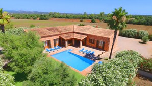 Eine Villa mit Swimmingpool, Liegestühlen und Garten.