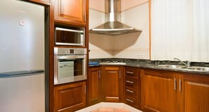 Una cocina con armarios de madera, una campana extractora de acero inoxidable, un microondas, un horno y un refrigerador.
