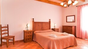 Ein Schlafzimmer mit einem hölzernen Bett, zwei Nachttischen, einem Schminktischchen, einem Sessel, einer Kommode und einem Spiegel an der Wand.