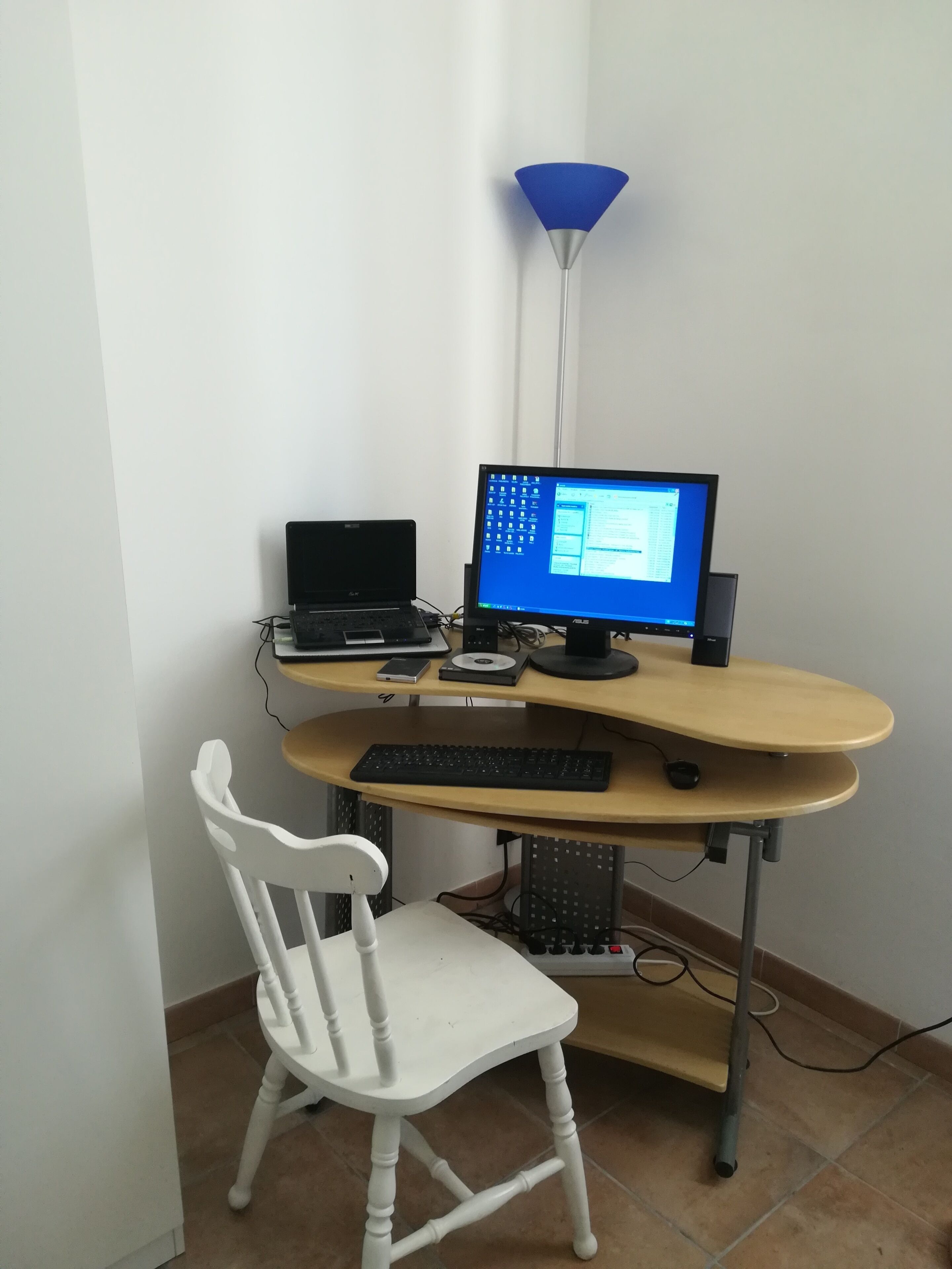 A computer desk with a monitor, keyboard, and a laptop. There is a white chair in front of the desk.