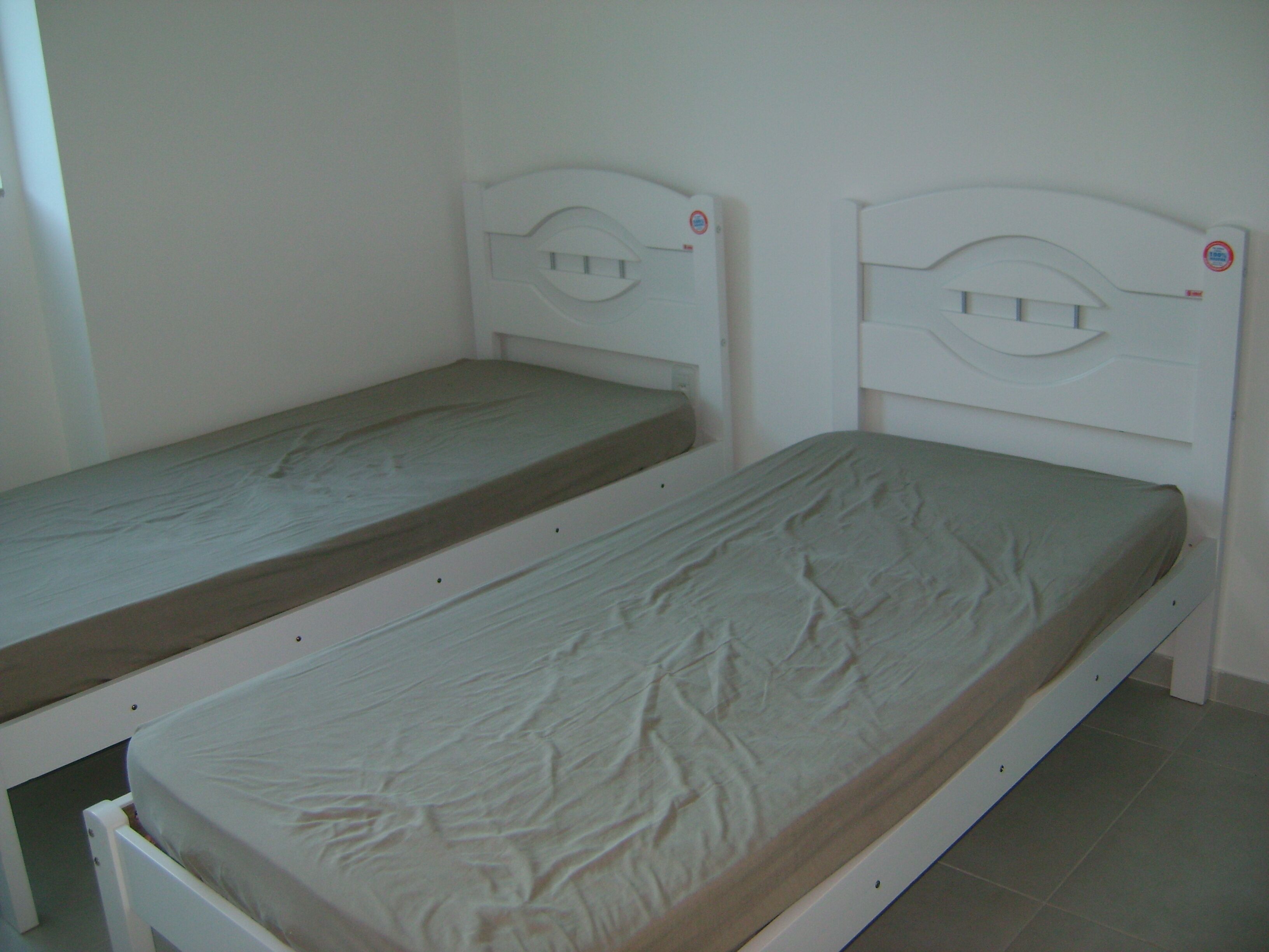 Two single beds with white headboards and a plain wall.