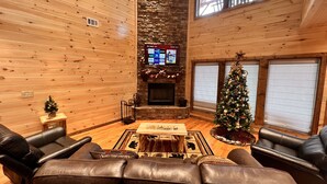 Accogliente interno di una baita in legno con camino, divani in pelle, un albero di Natale e una parete decorata in pietra.