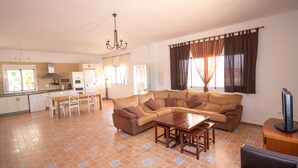 Una sala de estar con un sofá, una mesa de comedor y sillas. Hay una zona de cocina con armarios y un refrigerador.
