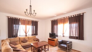 Una sala de estar con sofá, una mesa de centro, un televisor sobre un mueble bajo y cortinas en las ventanas.