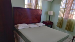 Un lit bien fait, avec une tête de lit en bois, une table de chevet avec une lampe et une fenêtre avec des rideaux.