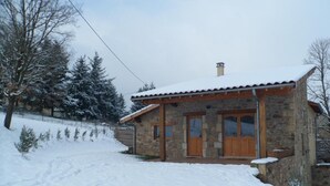 A stone house with a wooden door and windows, surrounded by snow-covered ground and trees. - Family cottage with terrace, pets welcome (Chuyer)