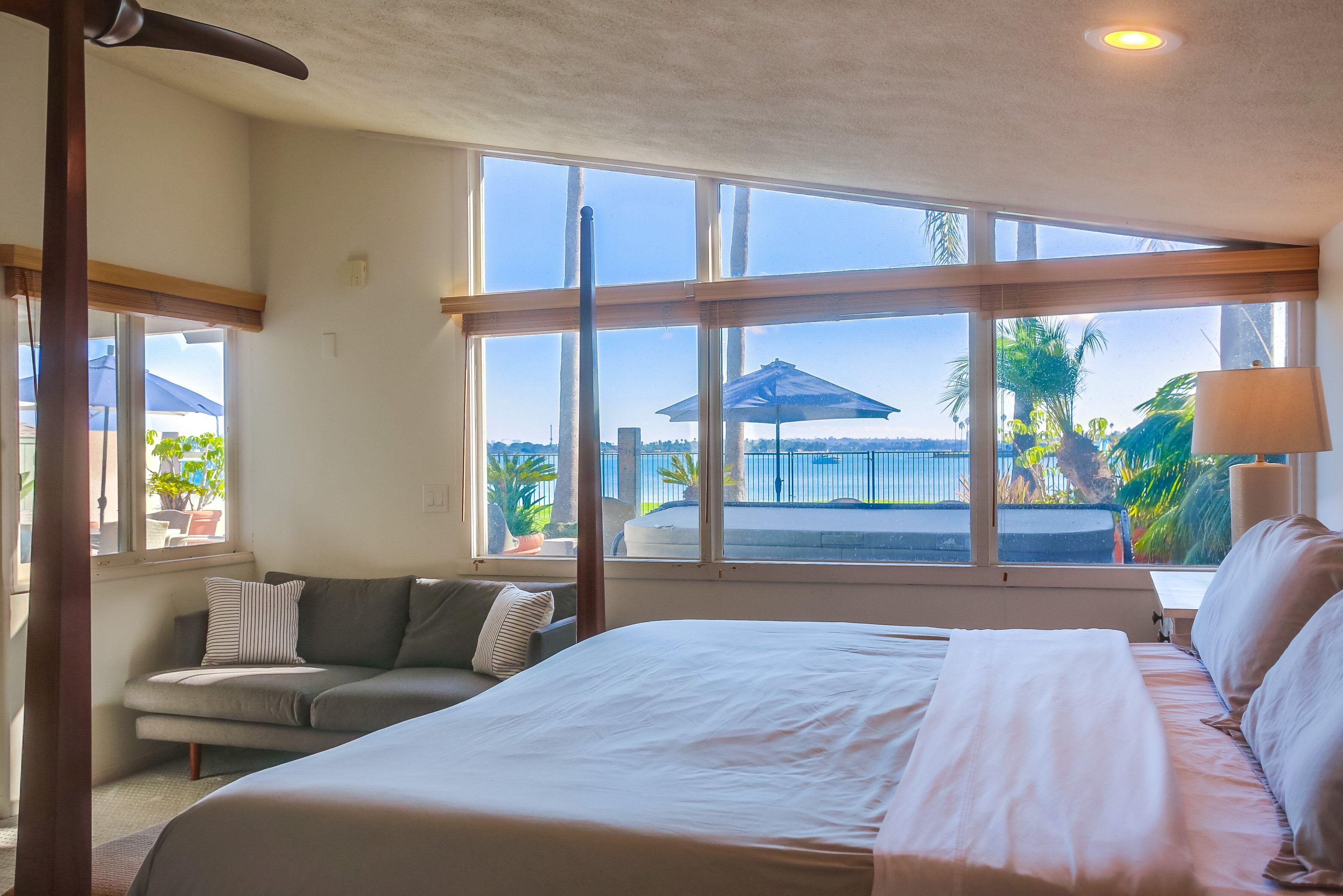 A bedroom with a large bed, a sofa, and a view of the outdoors through large windows.