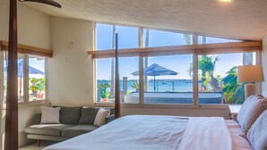 Ein Schlafzimmer mit einem großen Bett, einem Schlafsofa und Blick ins Freie durch große Fenster.