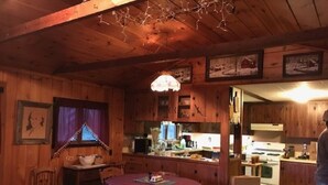Un interior de cabaña acogedor con una zona de comedor de madera, una cocina con estufa y una ventana con cortinas.