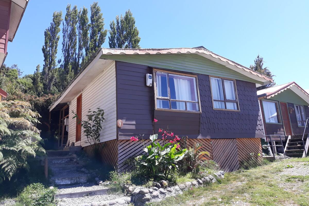 Une maison mobile de plain-pied, dotée d’un toit en pente, d’un porche à l’avant et d’un petit jardin agrémenté de rochers et de plantes.