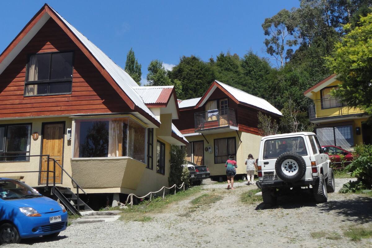Une rangée de cabanes, avec un chemin de terre qui y mène, un véhicule tout-terrain blanc garé devant, et une voiture bleue garée sur la gauche.