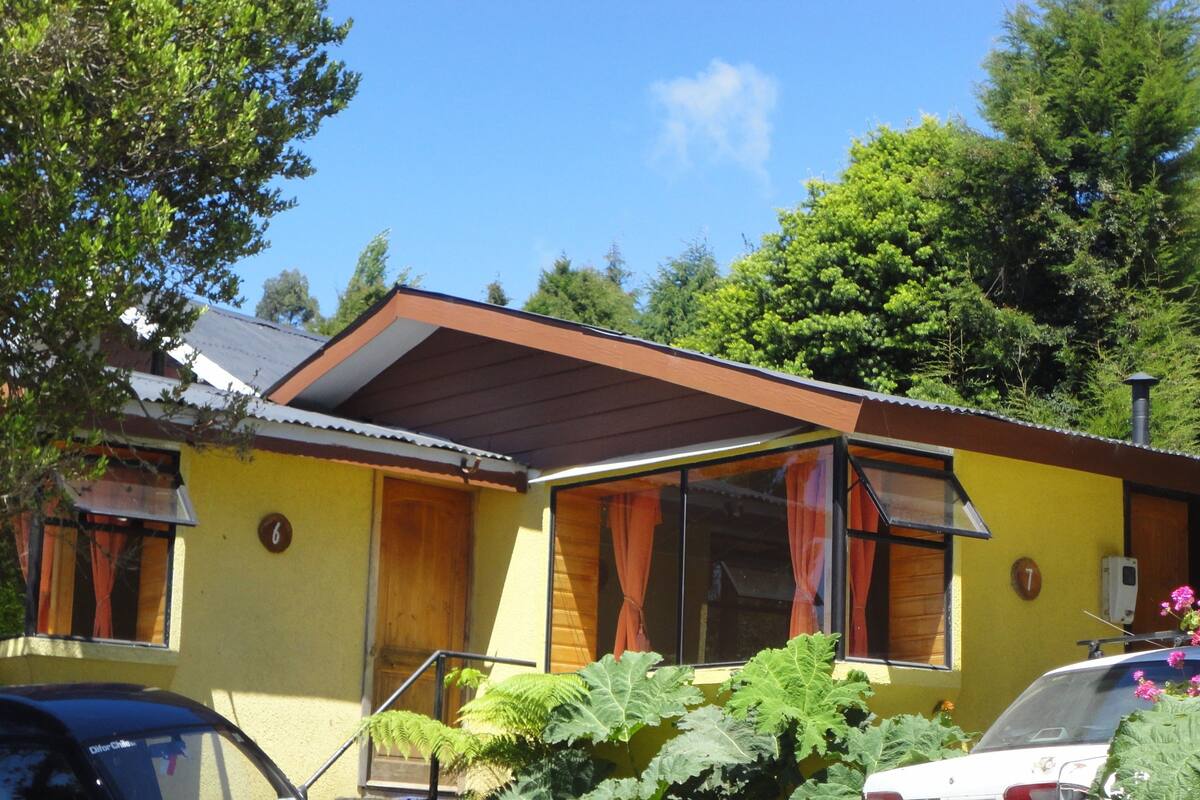 Un bâtiment jaune avec un toit marron, portant les numéros 6 et 7, et entouré de verdure.