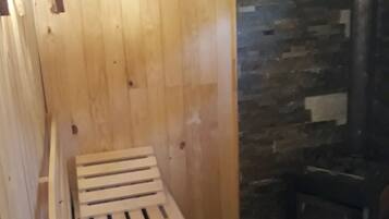 A wooden sauna with a bench, a stone wall, and a wood-burning stove.